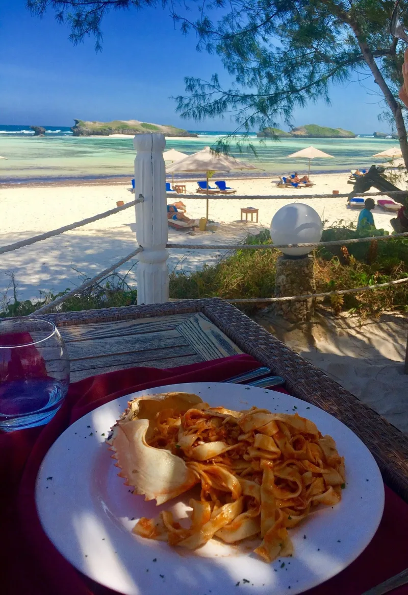 A plate of tagliatelle with crab, served with the shell on top, on a table overlooking loungers and the lagoon.
