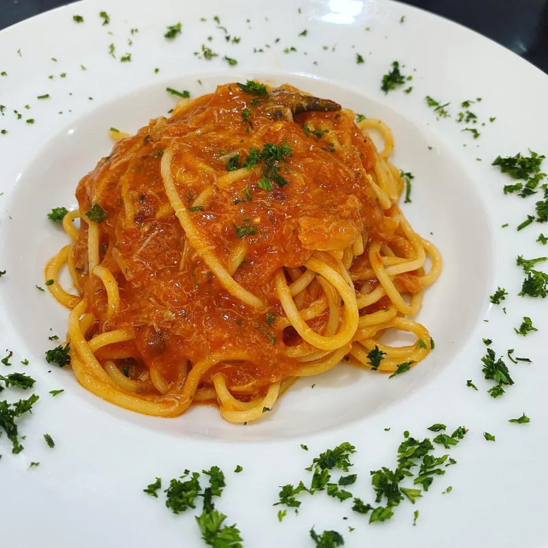 A plate of spaghetti in a rich tomato sauce, scattered with chopped parsley.
