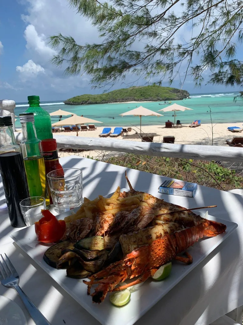 A plate of grilled lobster, prawns and calamari with chips and grilled vegetables, on a table looking out over umbrellas and the turquoise lagoon.
